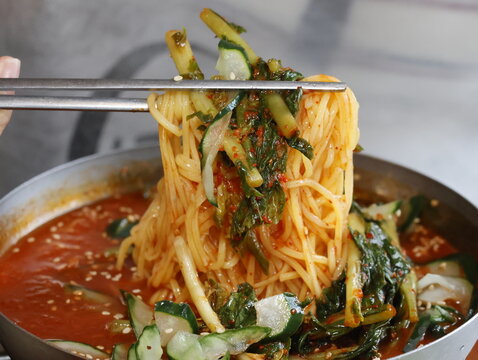 Korean cold kimchi noodles with vegetables in a bowl. The noodles are long and the vegetables are green