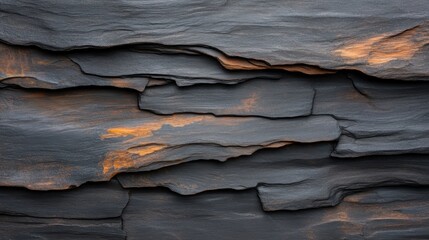 A close-up view of layered dark stone with warm orange highlights, showcasing the intricate...