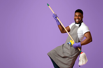 Portrait Of Funny Black Man In Apron With Mop In Hands Posing Over Pink Studio Background, Using...