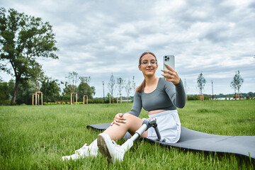 A young woman relaxes on a mat, capturing the moment outdoors with her prosthetic leg visible.