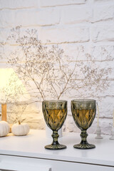  Home autumn composition.Charming green glassware with wine artfully combined with delicate decor of white pumpkins, lamp, dried branches on white bricks background.