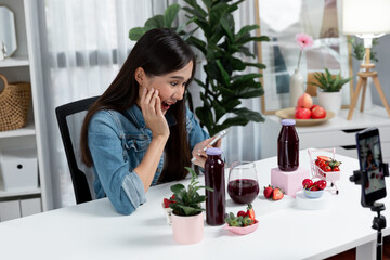 Smiling young beautiful Asian reviewing tasty mixed strawberry and cherry juice detox drinks, showing healthy product to promote for special promotion selling on social media online record. Stratagem.