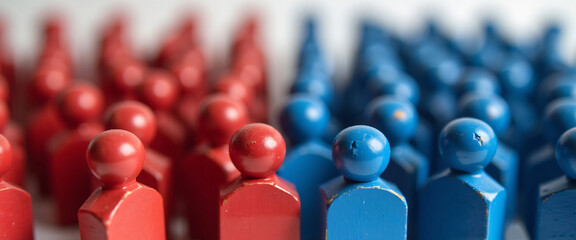 Painted red and blue wooden figures grouped together, symbolizing the divide between political parties or ideologies.

