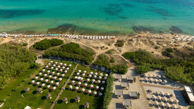 Aerial view of Pescoluse beach in Salento, Puglia, Italy. This beach is also called the Maldives of Salento. There are many umbrellas on the beach and tourists at the sea.