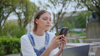 Focused student browsing mobile phone sitting street cafe with laptop closeup.
