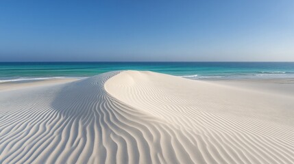 A panoramic view of a white sand dune with rippled patterns, stretching towards a vast turquoise ocean under a clear blue sky.