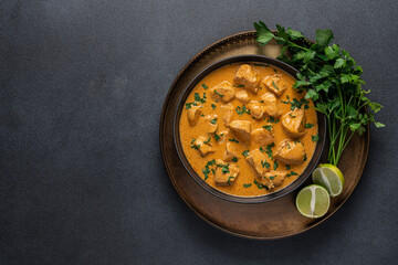 Chicken curry in black bowl with green herbs and lime on  dark background with copy space. Traditional asian food