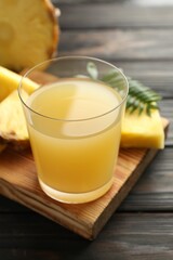 Tasty pineapple juice in glass and slices of fresh fruit on wooden table, closeup