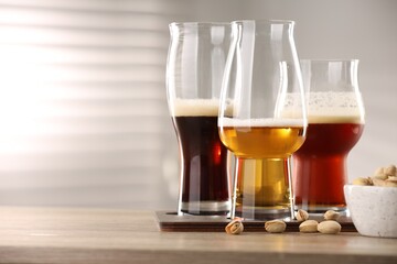 Glasses with different types of beer and pistachio nuts on wooden table indoors, space for text
