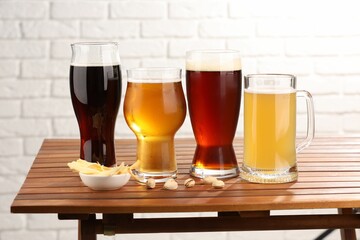 Glasses with different types of beer and snacks on wooden table against white brick wall