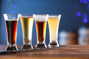Glasses with different types of beer on wooden table against blue background, closeup