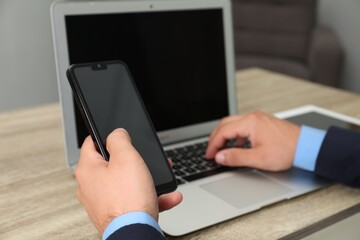 Businessman using smartphone and laptop at wooden table, closeup. Modern technology