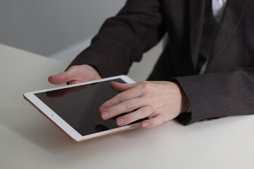 Businessman using tablet at white table indoors, closeup. Modern technology