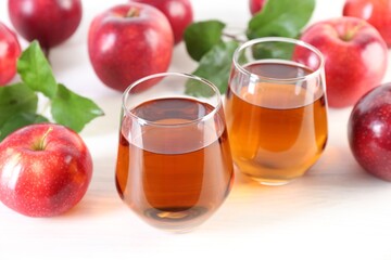 Fresh apple juice in glasses, fruits and green leaves on white table, closeup