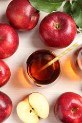 Fresh apple juice in glass, fruits and green leaves on white wooden table, flat lay