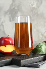 Fresh apple juice in glass and fruits on light grey table