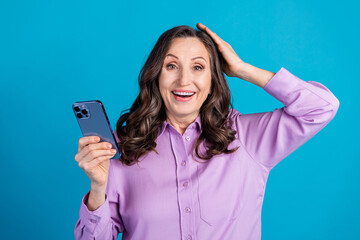 Photo of impressed positive woman wear violet shirt getting likes modern device empty space isolated blue color background