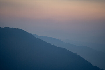 Fototapeta premium As dawn broke, the mist rose from the vale, revealing a breathtaking landscape where mountains kissed the sky, hills framed the view, and trees danced in the morning fog.