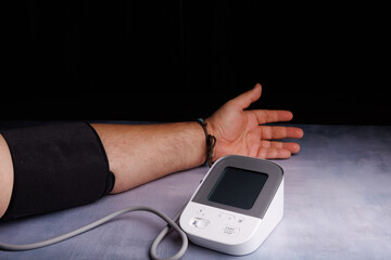 Close-up of a person using a digital blood pressure monitor on a concrete table, showcasing heart health and wellness in a medical setting