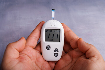 Glucometer in a person's hands revealing test results on a concrete surface, highlighting the...