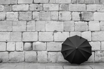 Black umbrella against rustic stone wall in monochrome setting
