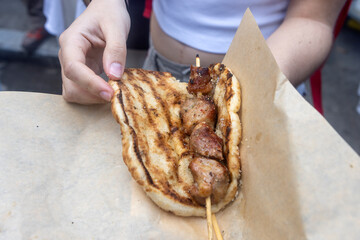 A person is holding a grilled pita wrapped around a skewer of grilled meat.