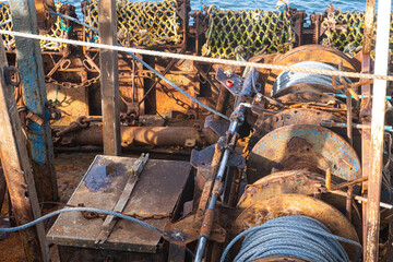 Winching machinery with signs of corrosion. Close-up of machinery for winching nets on a fishing boat. The rusting mechanism has ropes attached, and nets are hanging over the side of the boat