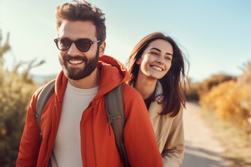 Fototapeta premium A cheerful couple strolls through a scenic outdoor area, smiling at each other under the bright sun, surrounded by lush foliage. Their relaxed vibe radiates happiness