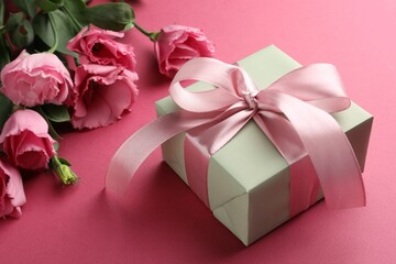 Beautiful gift box with bow and eustoma flowers on pink background, closeup
