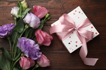 Gift box with bow and flowers on wooden table, flat lay