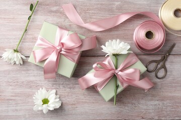 Gift boxes with bows, ribbon, scissors and flowers on pink wooden table, flat lay