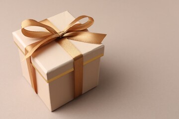 Gift box with golden bow on beige background, closeup. Space for text