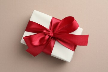 Gift box with red bow on beige background, top view