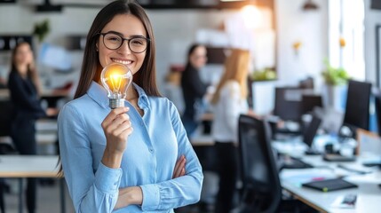 A Woman in a Blue Shirt Holding a Lit Lightbulb in an Office Setting