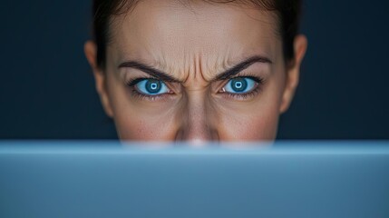 Businesswoman s face in closeup, with a deep frown, lit by her laptop screen, symbolizing frustration and digital overload