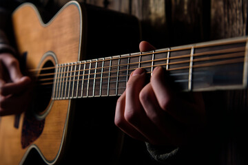 Fototapeta premium Closeup of hands playing an acoustic guitar in a dimly lit setting, highlighting the strings and frets with a focus on musical expression