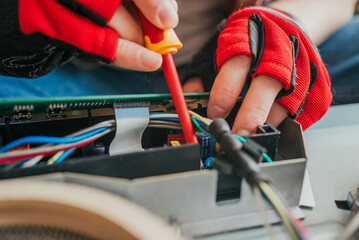 Electrician in gloves works meticulously on a circuit board, connecting wires with a screwdriver....