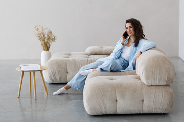 Obraz premium Happy beautiful woman is talking on a phone sitting on a sofa at home.