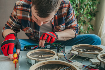 Focused electrician repairs burner element on electric stove top with screwdriver, ensuring safety and efficiency