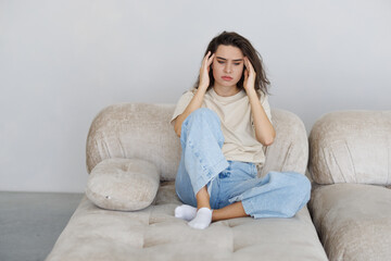 Stressed young woman suffering migraine and complaining sitting on a couch at home