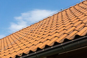 Vintage orange ceramic roof tiles. Tiled roof texture. Blue sky over the house. Structure rooftop's peak. Lightning rod running along the roof. Blue cloudy sky over cottage house. Roofing industry.