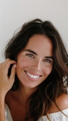 Fototapeta premium Brunette woman smiling while touching her face against a plain white background in a close-up shot with professional lighting