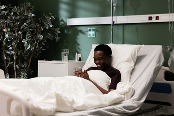 Young African patient clutches her phone, using to escape momentarily from the confines of her illness.