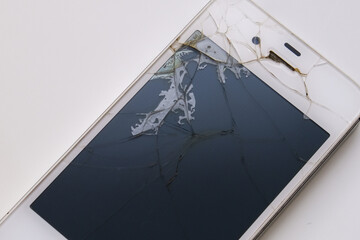 A broken cell phone with a cracked screen on a wooden table