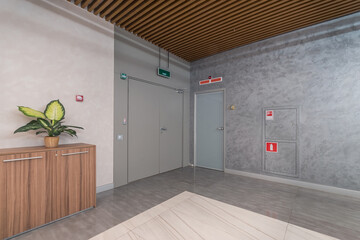 The hall of the office floor with a potted plant on the cabinet and a green emergency exit .sign...
