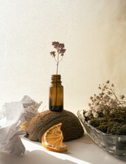 A frosted bottle with a dry branch of flowers inside stands on a coconut. White paper and a dried...