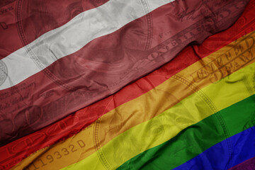 waving colorful flag of latvia and gay rainbow flag on the dollar money background. finance concept.