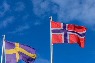 Flags of Norway and Sweden billow against a brilliant blue sky on a sunny day, representing unity and shared heritage in Northern Europe