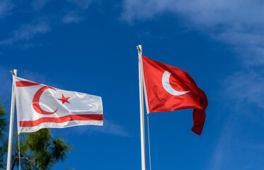 Flags of Turkish Republic of Northern Cyprus and Turkey waving against a bright blue sky in a serene atmosphere