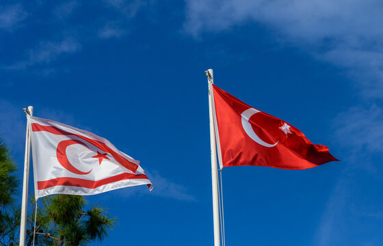 Turkish and Turkish Republic of Northern Cyprus flags waving proudly against a clear blue sky in a coastal location during a sunny day